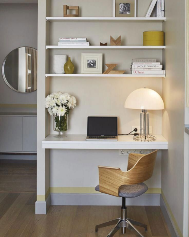 A office desk built in the wall, with shelves and decoration. Mirror can also be seen in the background. 